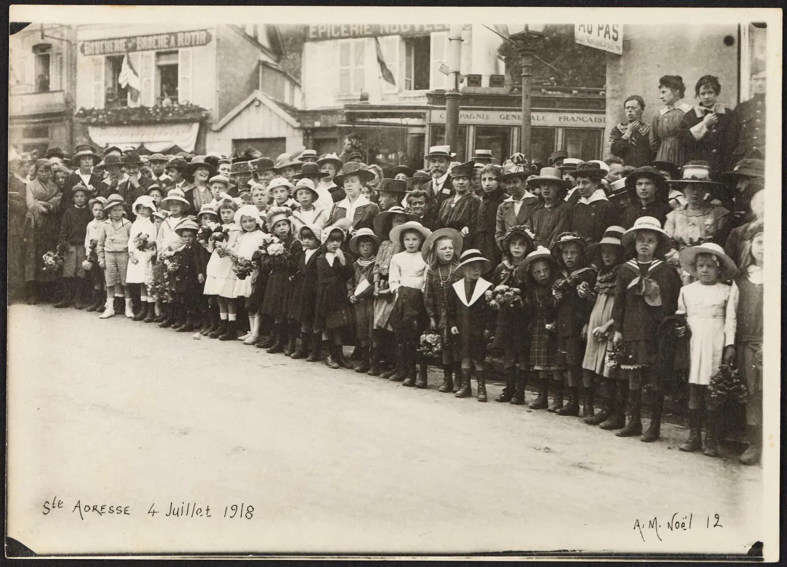 [Enfants avec des bouquets de fleurs, massés le long de la route d'Octeville à…
